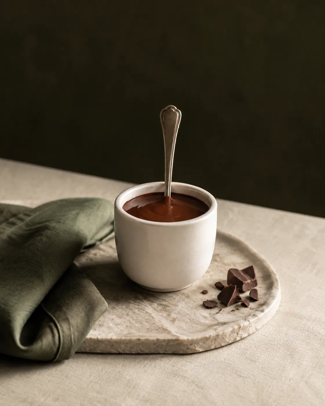 A small cup of thick dark drinking chocolate with a spoon standing in it