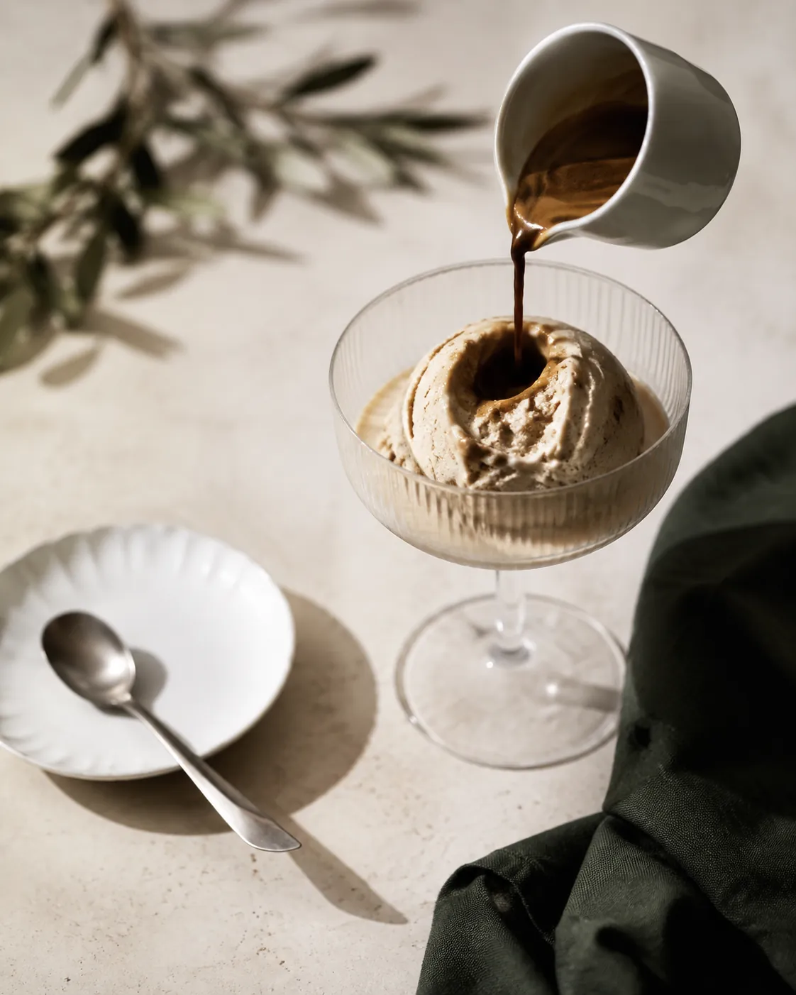 A small espresso cup tipped over a chilled glass of ice cream, the dark stream landing in a hollow on the scoop