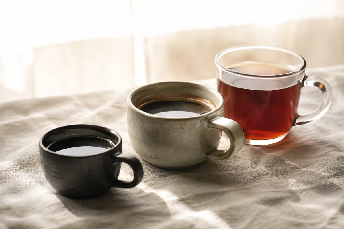 Three cups of black coffee backlit in a row, the left small and very dark, the middle longer and paler with a thin crema ring, the right a clear bright filter coffee