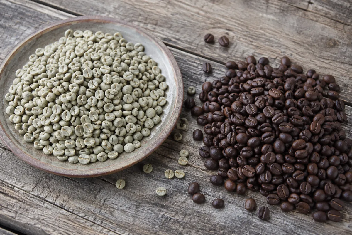 Pale green unroasted coffee beans in a shallow dish beside darker roasted decaf beans