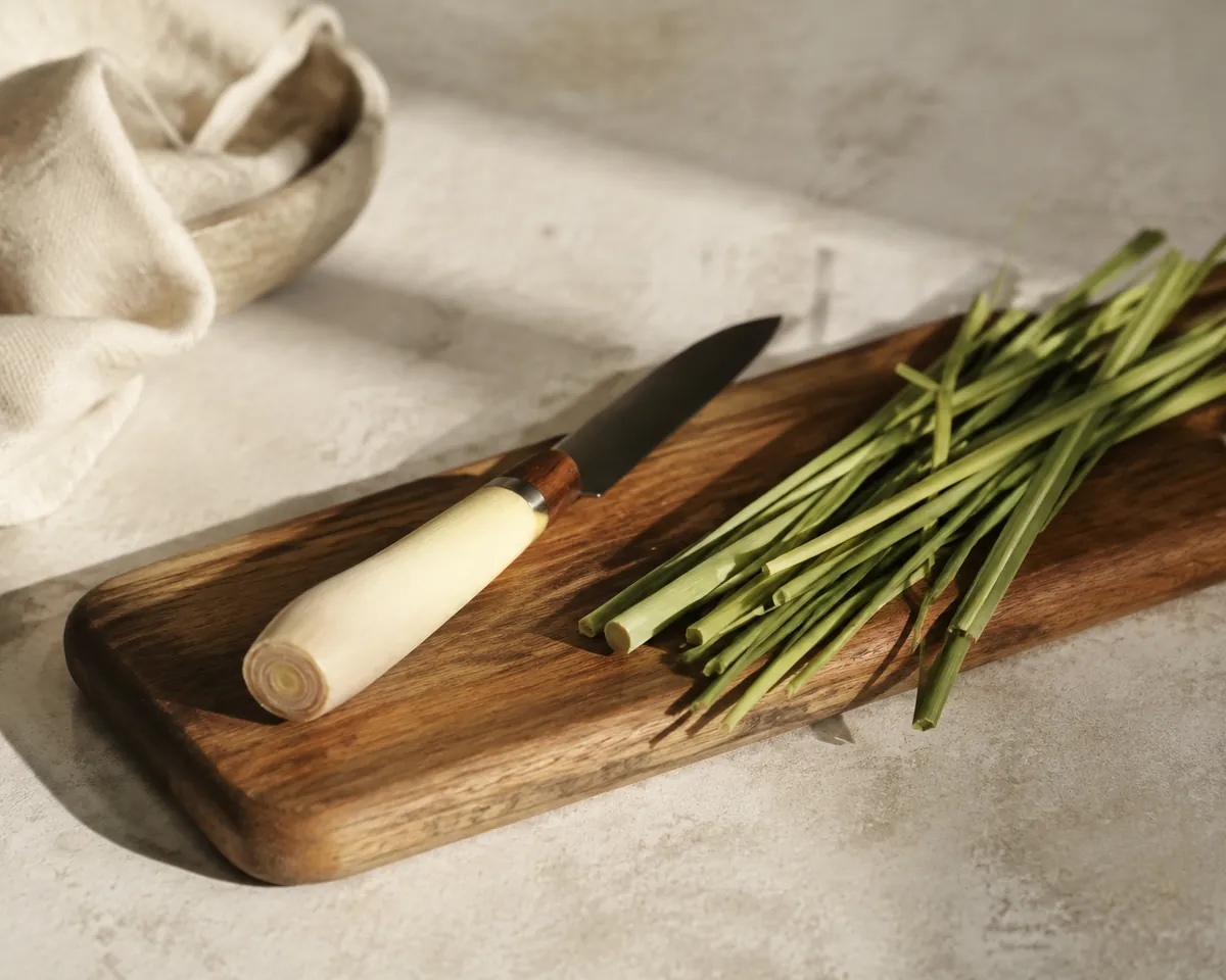 A lemongrass stalk cut in two on a board, the pale trimmed base on one side and the discarded green upper leaves on the other