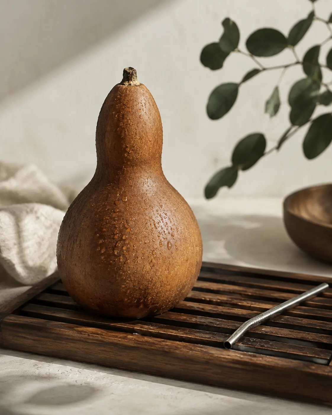 A rinsed natural gourd standing mouth-down on a wooden rack to drain, a metal straw drying beside it