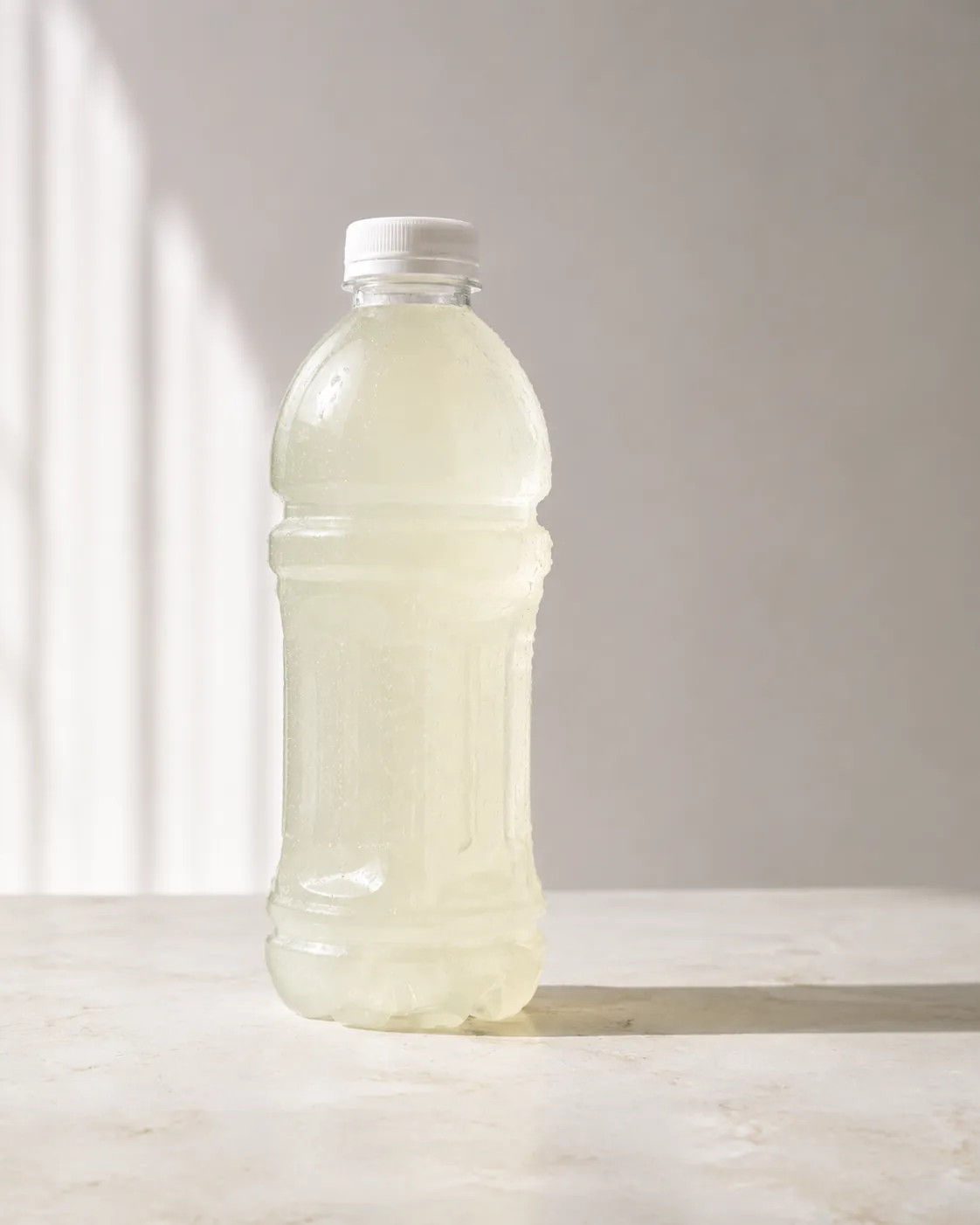 A clear bottle of pale coloured sports drink on a pale stone surface