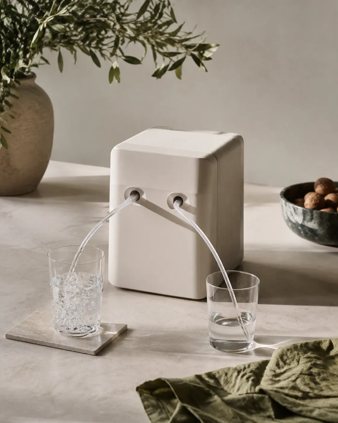 A plain countertop water ioniser with two tubes running into two glasses, one filling and the other draining, on a pale worktop