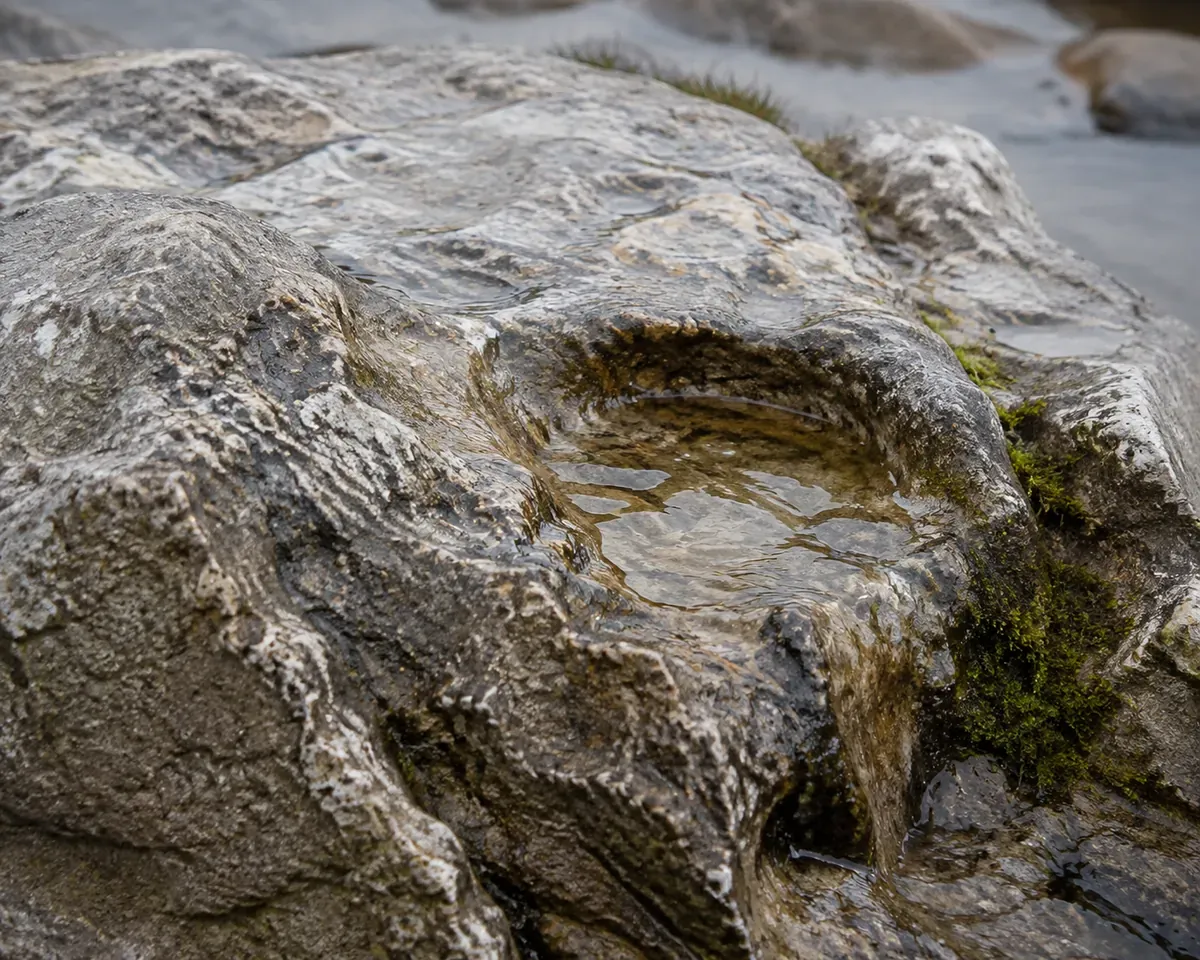 Weathered pale limestone with water running over it and pooling in a small hollow, moss at one edge, in overcast daylight