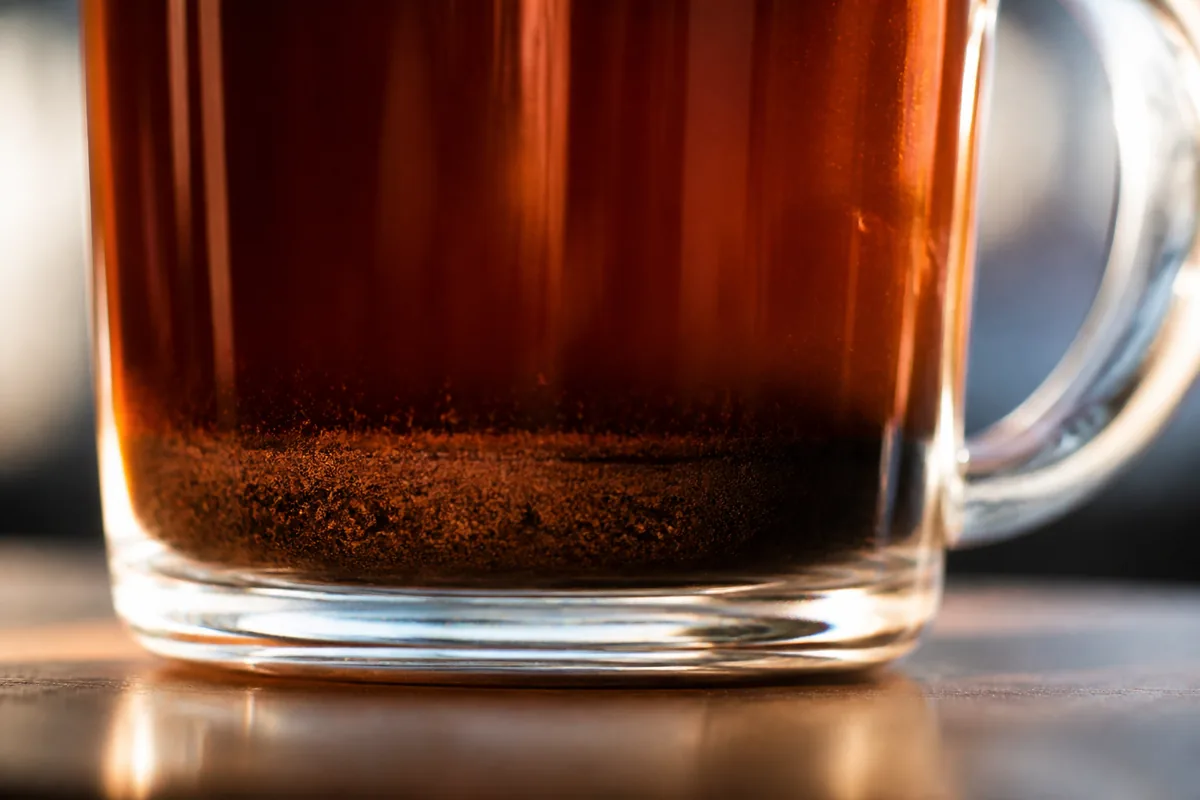 The bottom of a clear glass cup of French press coffee showing fine sediment settled in the base