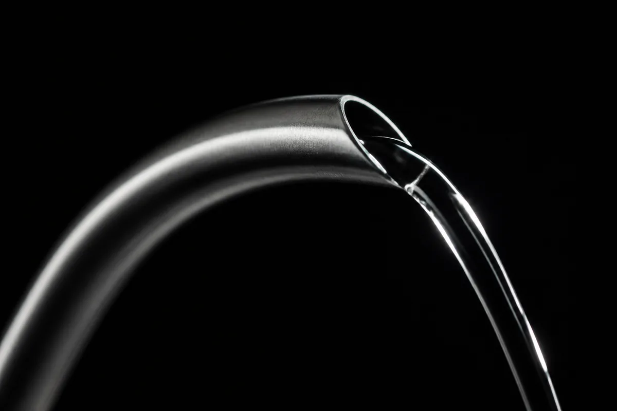 The curved spout of a gooseneck kettle in close macro with a thin controlled stream of water leaving it