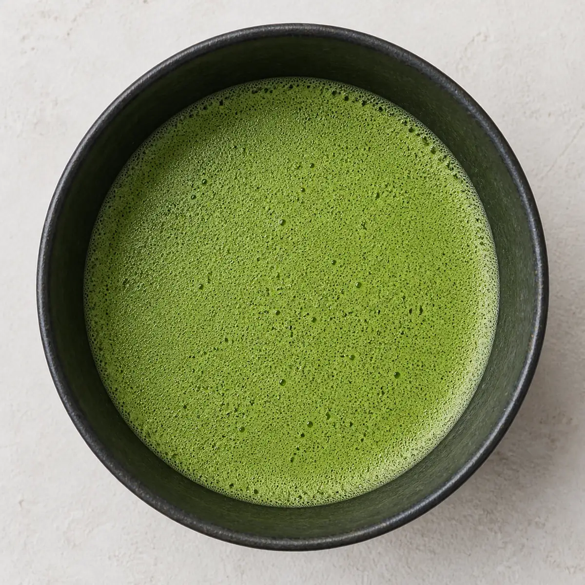 A ceramic bowl of freshly whisked matcha with a dense fine foam covering the surface, seen from directly above