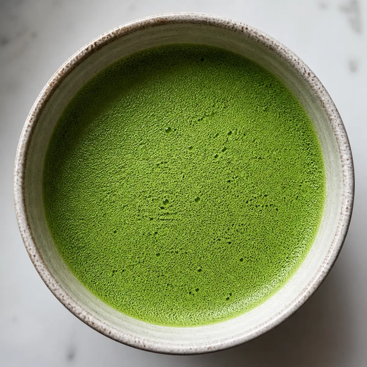 A bowl of whisked matcha seen from above with the powder fully suspended and a fine foam across the surface