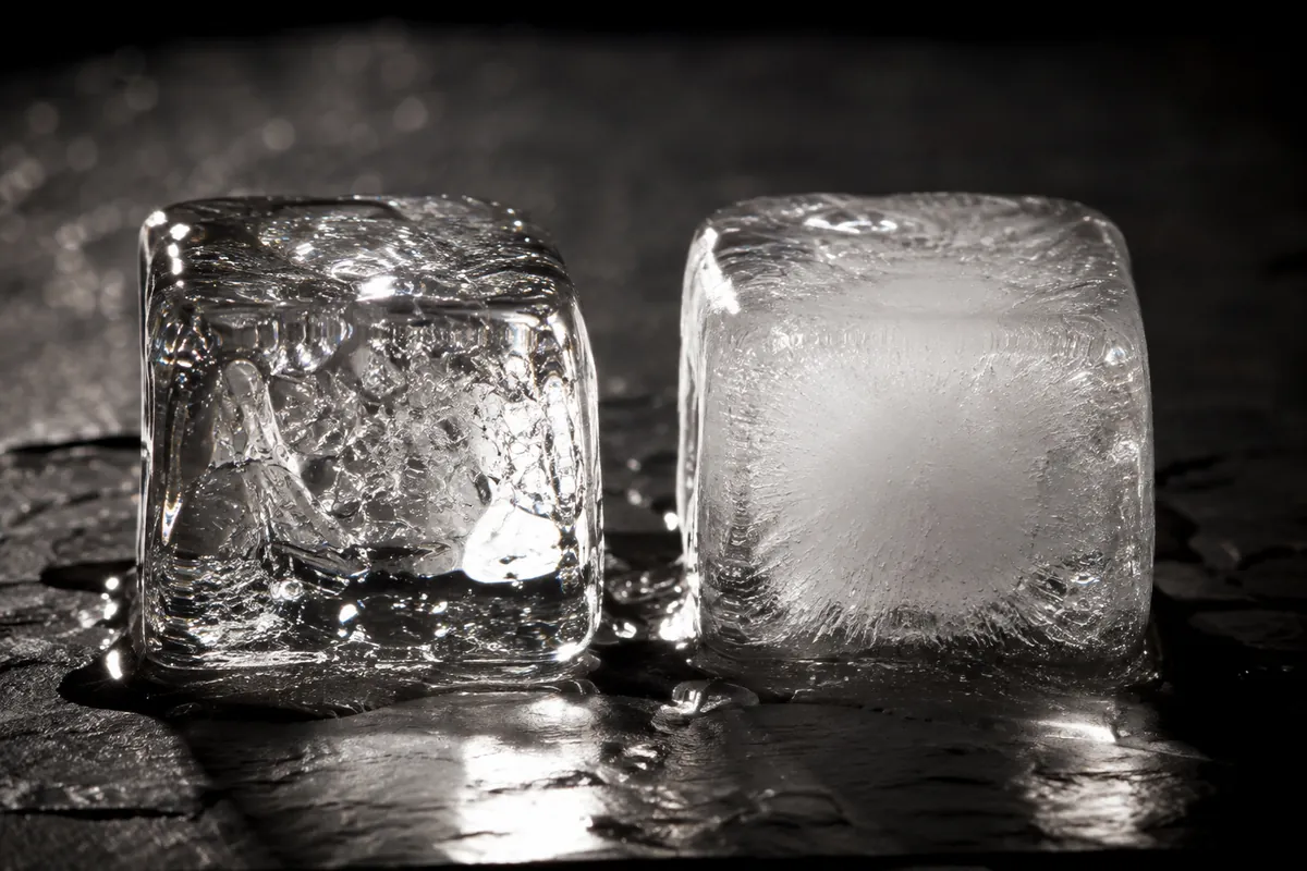 Two backlit ice cubes on dark slate, the left perfectly transparent and the right with an opaque white cloudy core