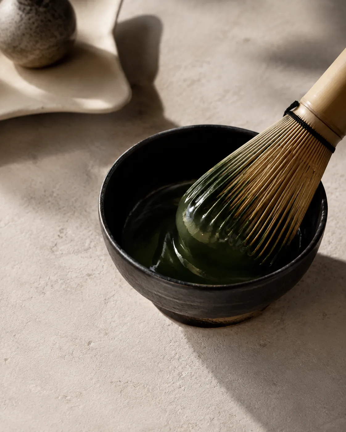 A small bowl of thick glossy dark green tea being folded with a bamboo whisk, no foam on the surface