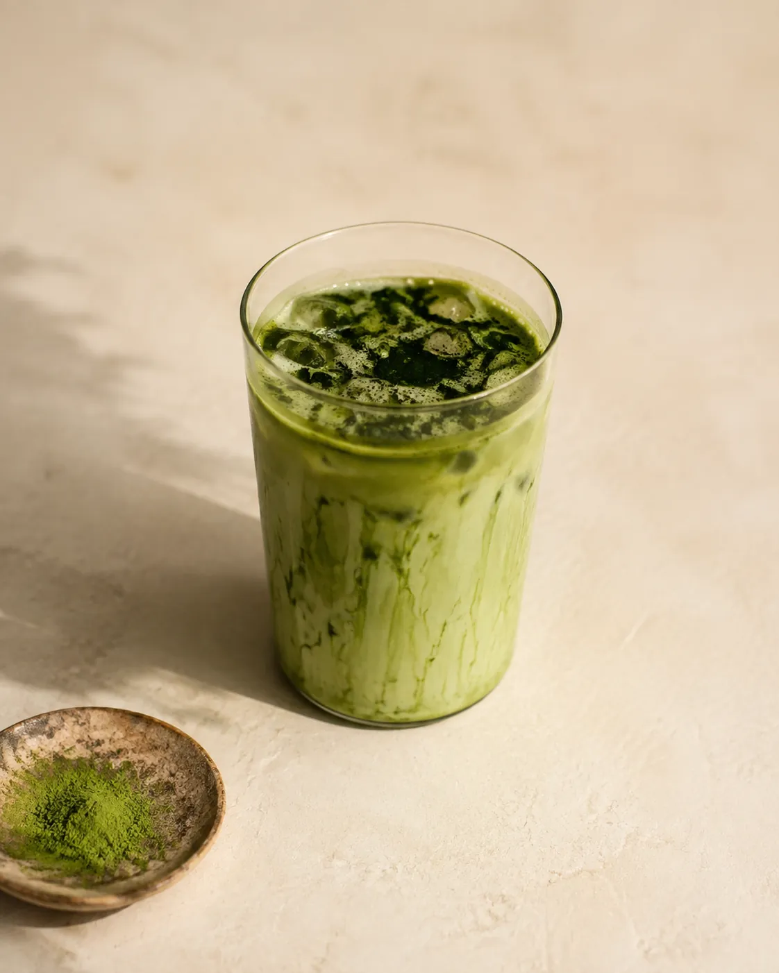 A glass of cold matcha with dark green clumps of undispersed powder floating on the surface and clinging to the sides