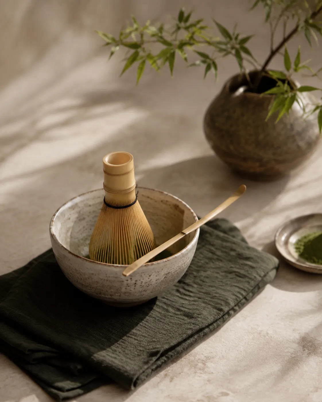 A wide ceramic bowl with a bamboo whisk standing in it and a bamboo scoop resting across the rim