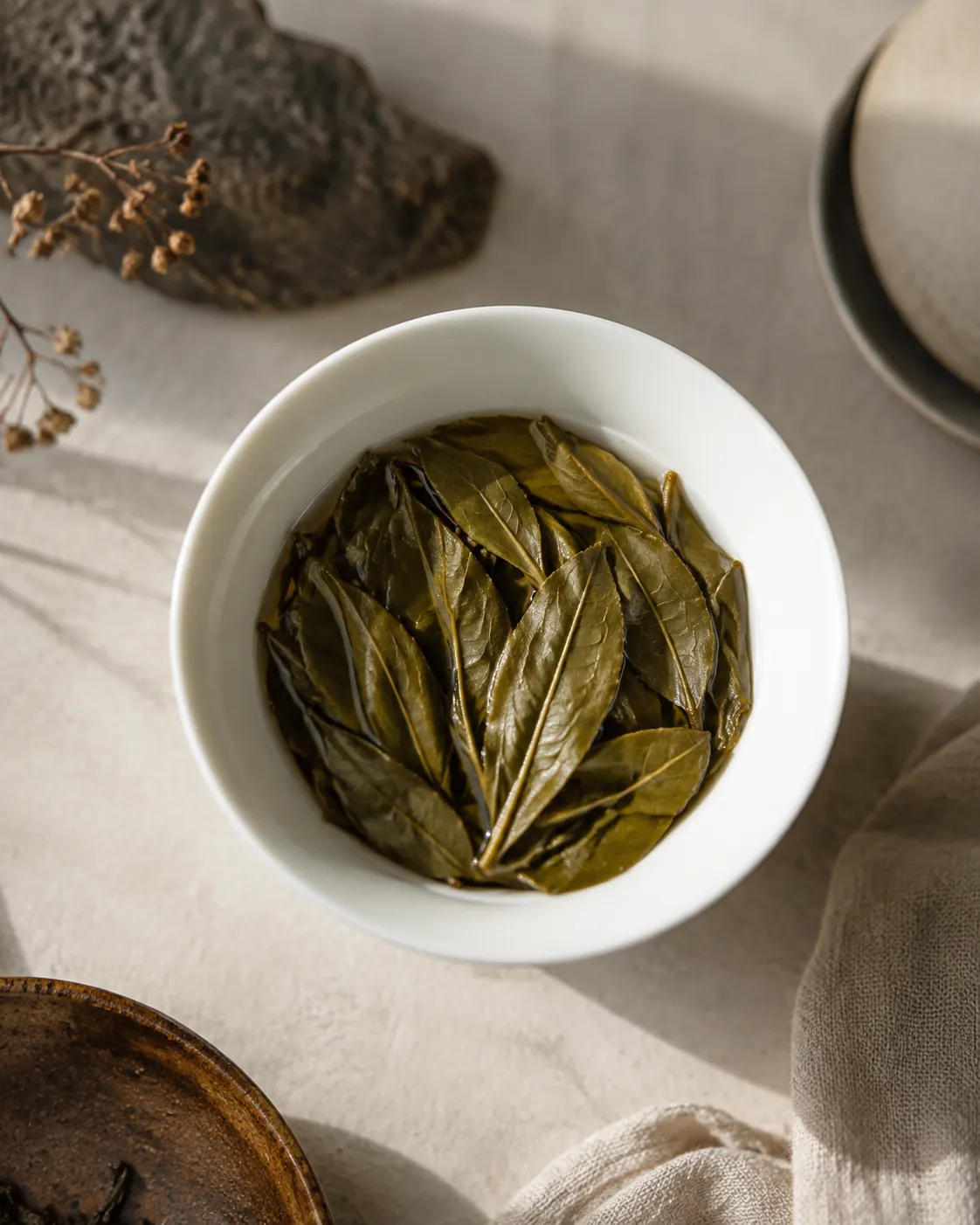 An open gaiwan of fully unfurled wet tea leaves after brewing, the leaves whole and olive green against white porcelain