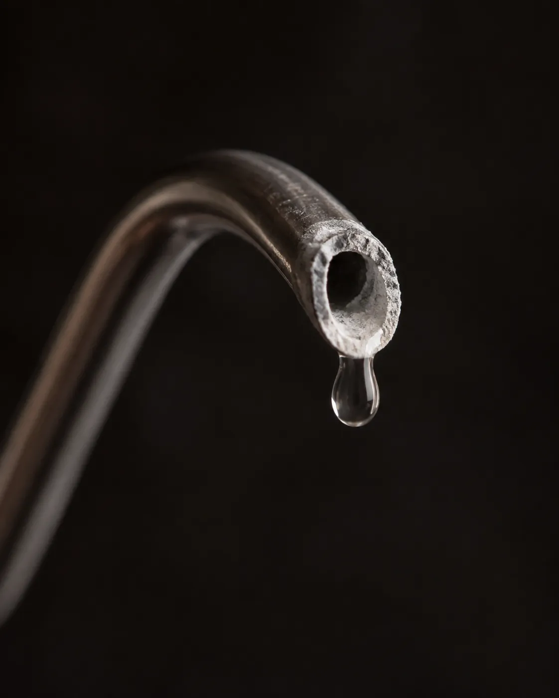 Close view of a gooseneck spout tip with chalky white limescale around the bore