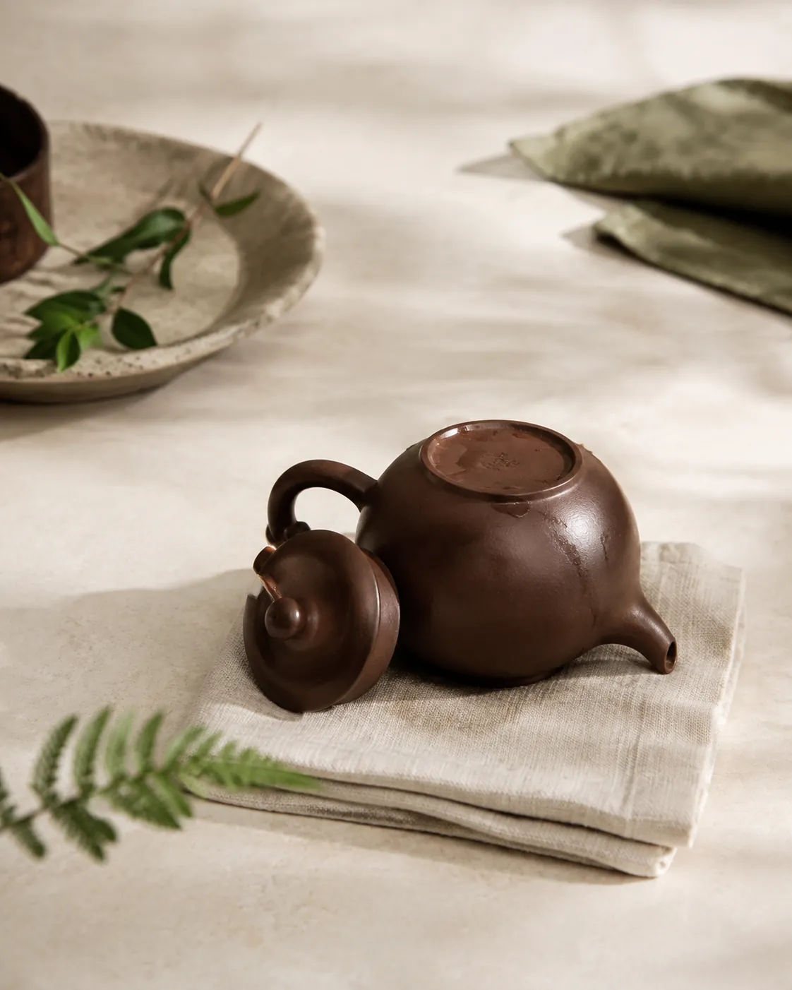 A small teapot standing upside down on a folded cloth to drain with its lid propped alongside