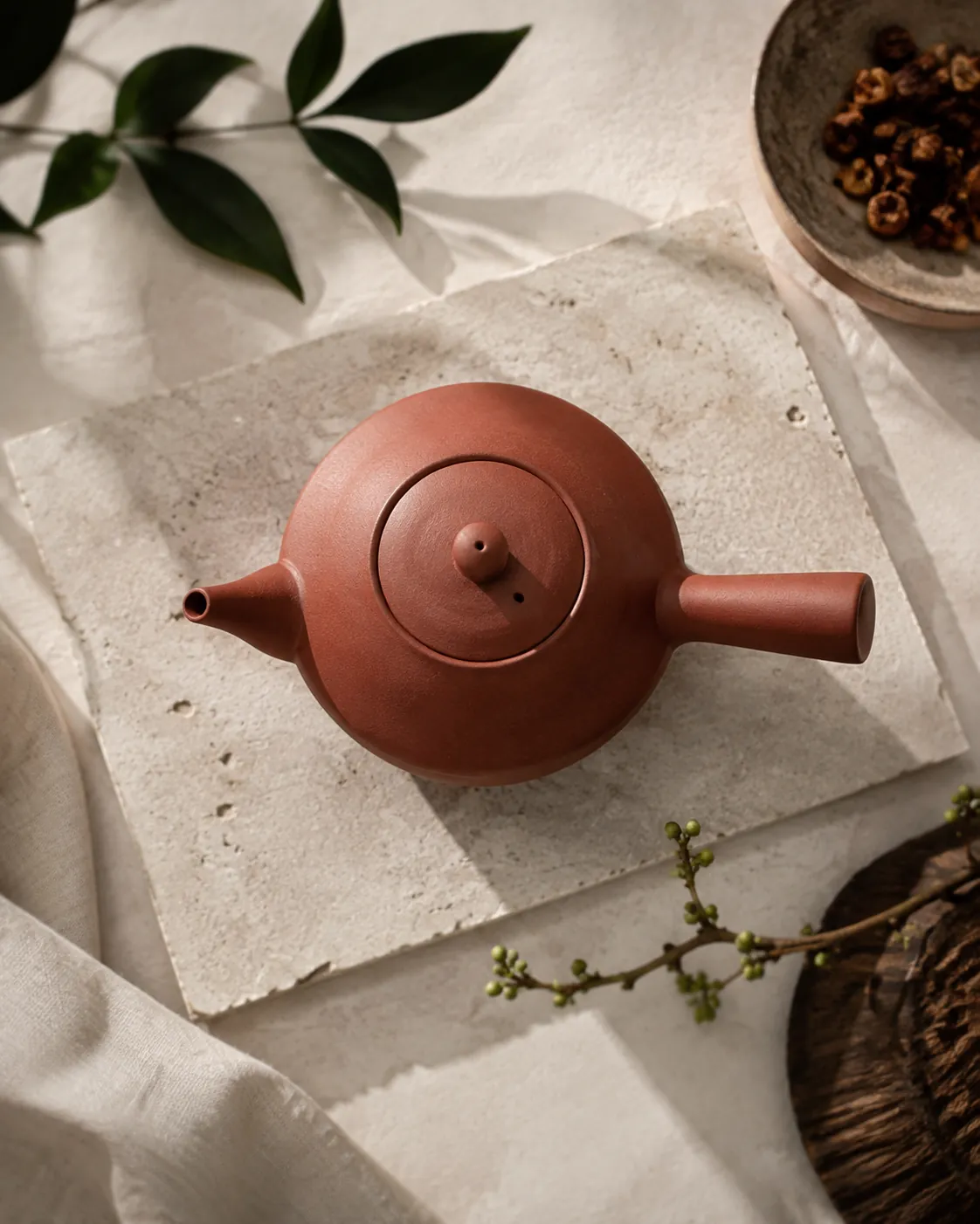 A small unglazed red clay teapot seen from above with its cylindrical handle projecting at a right angle from the spout