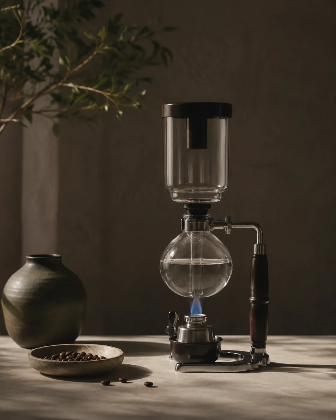 A siphon brewer standing on its frame above a small butane burner, the flame narrow and blue beneath the glass globe