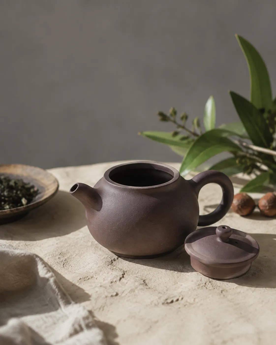 A small unglazed reddish-brown Yixing teapot with its lid off, the matt bare clay surface catching low side light