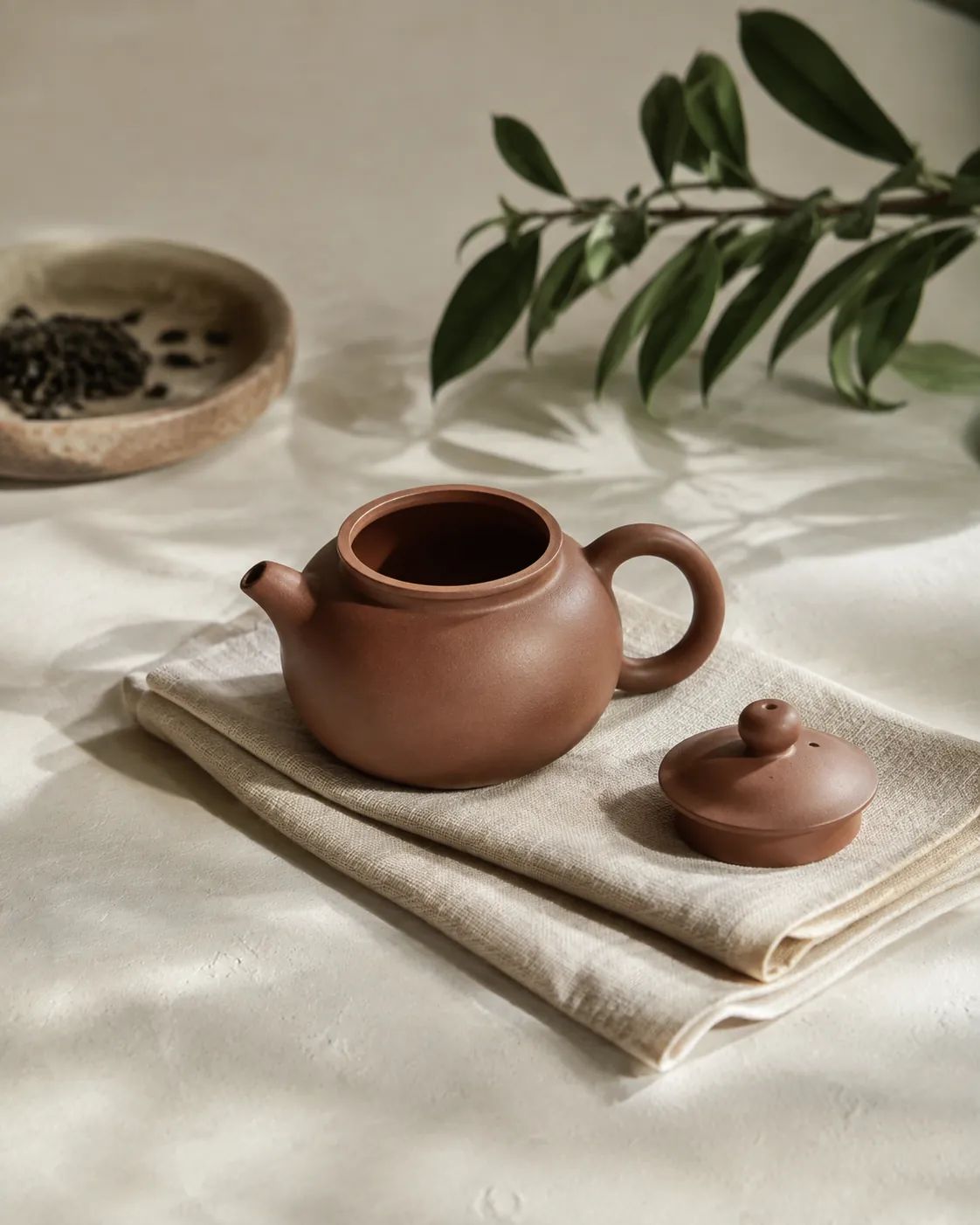 A small clay teapot standing on a folded cloth with its lid resting beside it, drying in daylight