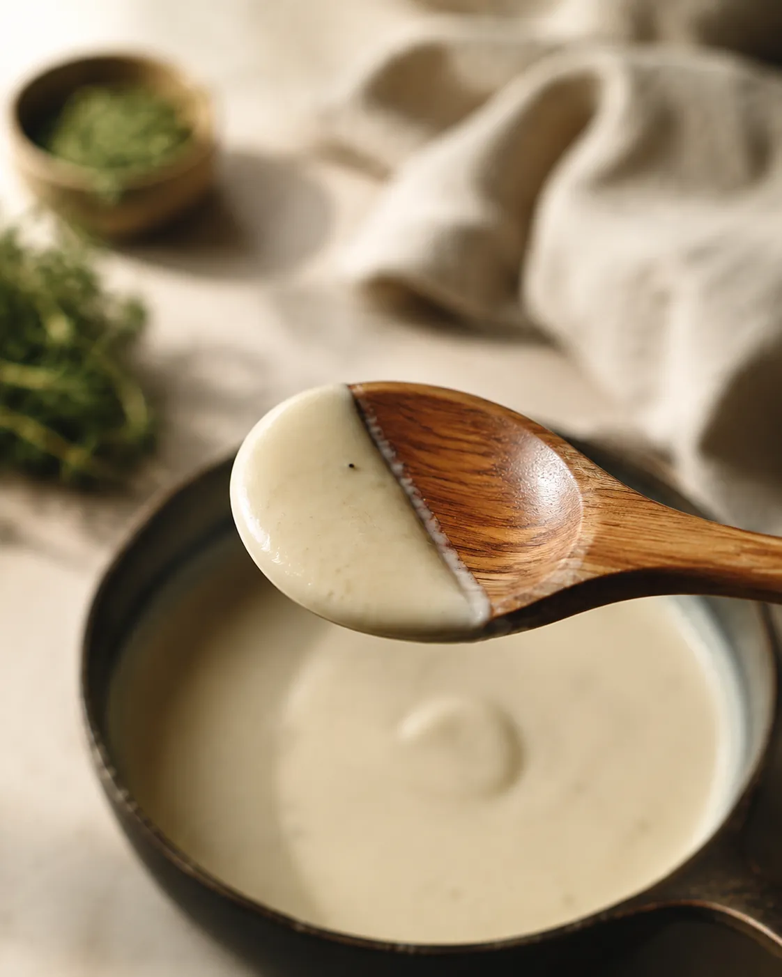 A wooden spoon lifted from a pan of pale thickened sauce, the coating holding on the back of the spoon