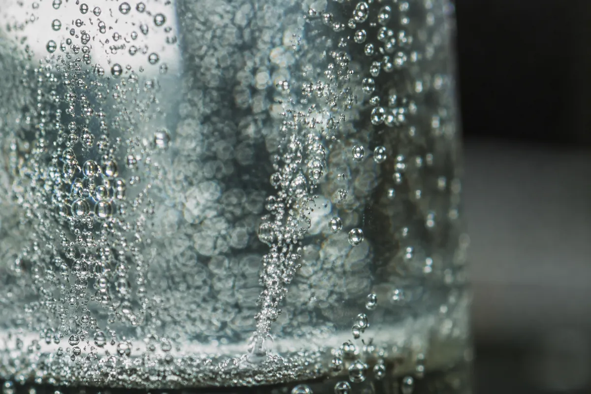 Extreme close macro of fine bubbles clinging to the inside of a glass and rising in a stream from a single point