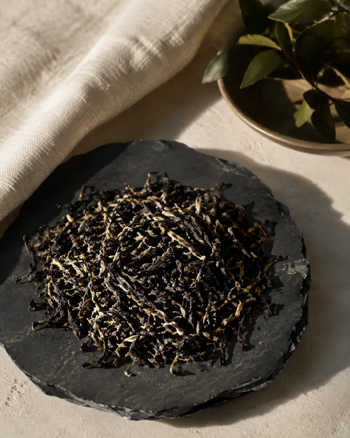 A close overhead view of dry black tea leaf on dark slate, heavily flecked with pale downy golden buds