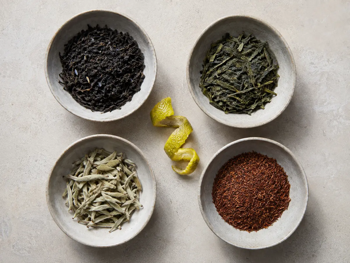 Black, green, white, and rooibos Earl Grey leaves arranged with fresh bergamot peel