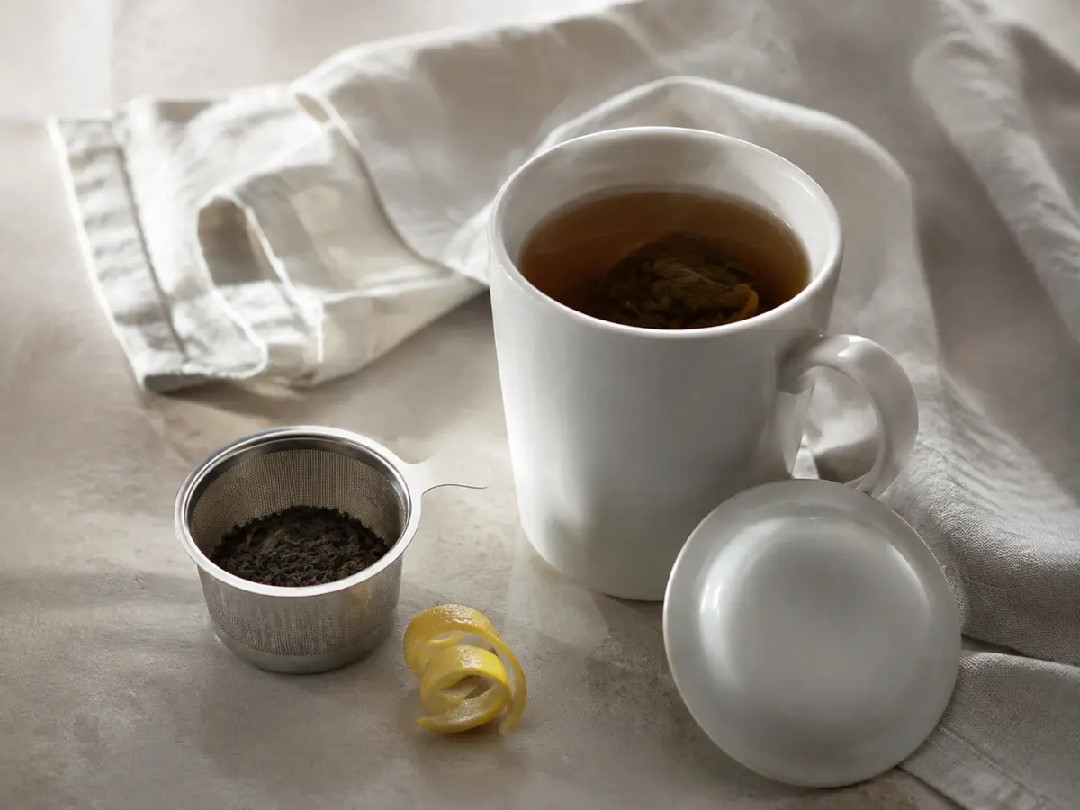 Covered porcelain Earl Grey mug beside loose black tea and a curl of bergamot peel