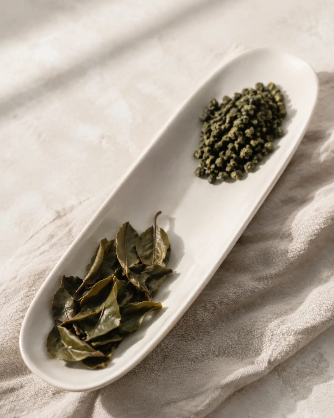 Tightly rolled dry oolong pellets on the left of a white dish and the same leaves fully unfurled and wet on the right